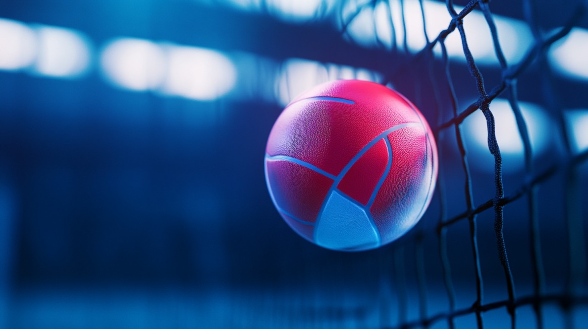 A close-up of a red and blue volleyball caught in the net, with a blurred indoor court in the background under blue lighting