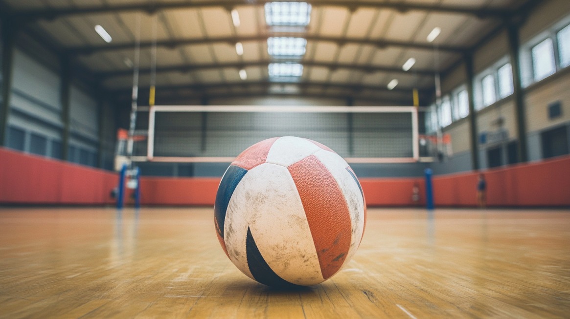 A close-up of a slightly worn volleyball on a polished indoor court with a net in the background